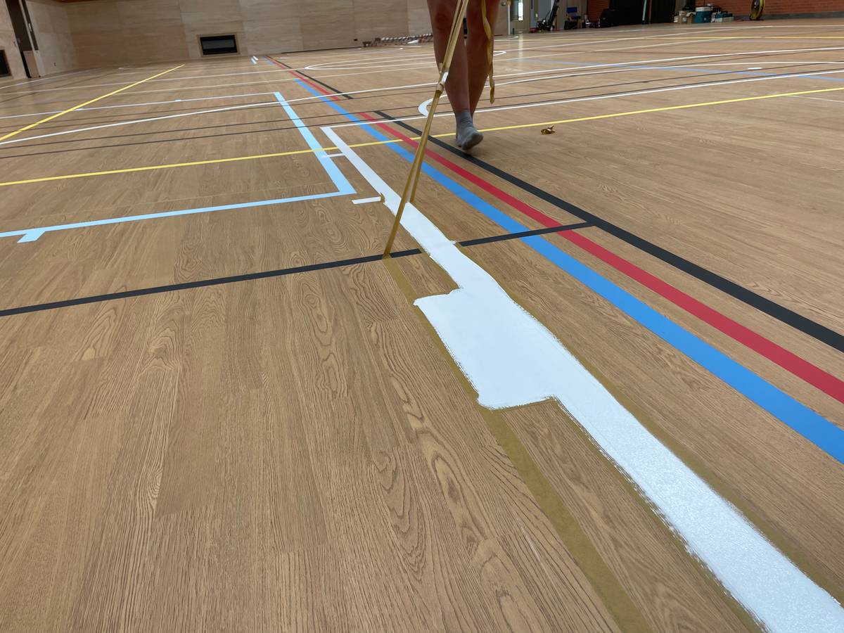 Painting a court line by hand on a sports hall floor