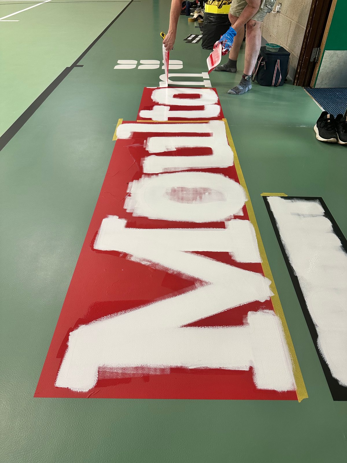 Painting the Moulton logo onto a green sports floor
