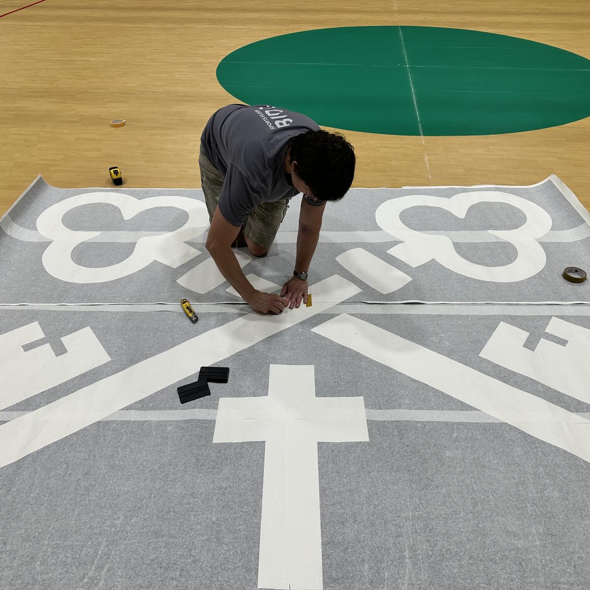 Preparing a school crest stencil on a sports hall floor