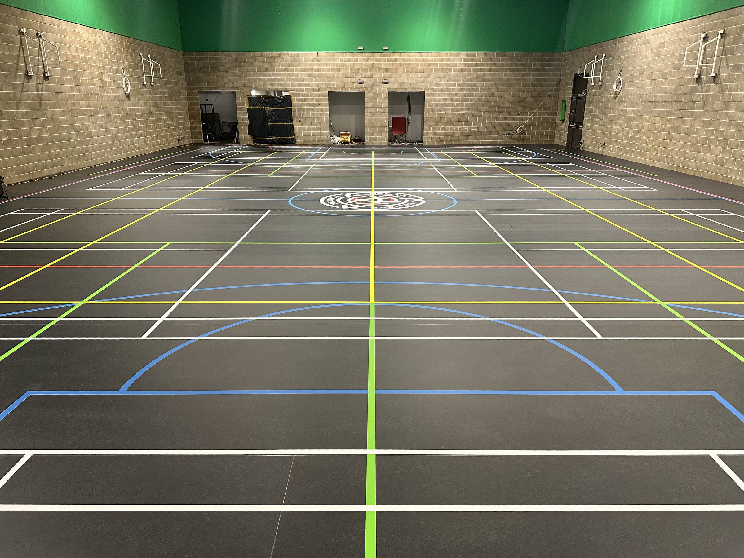 Sports hall with colour-coded multi-sport court markings and a school crest in the centre circle